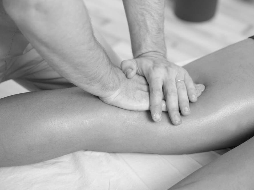 Black and white image of a massage therapist applying pressure with one hand on top of the other on the back on a clients left knee.
