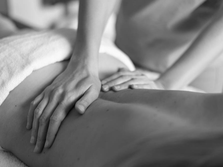 Black and white image of a massage therapist using Swedish body massage techniques, with both hands on the lower back of a client who is lying face down.