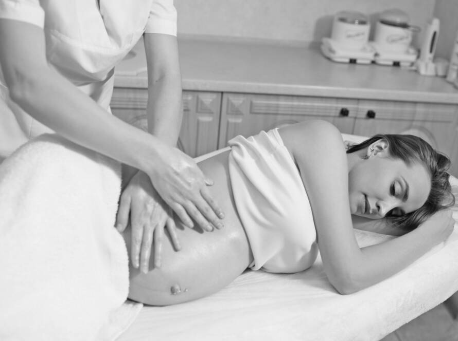Black and white image of a pregnant woman laid on her side, while the massage therapist uses soft and gentle strokes on the side of the clients abdomen during a pregnancy massage.