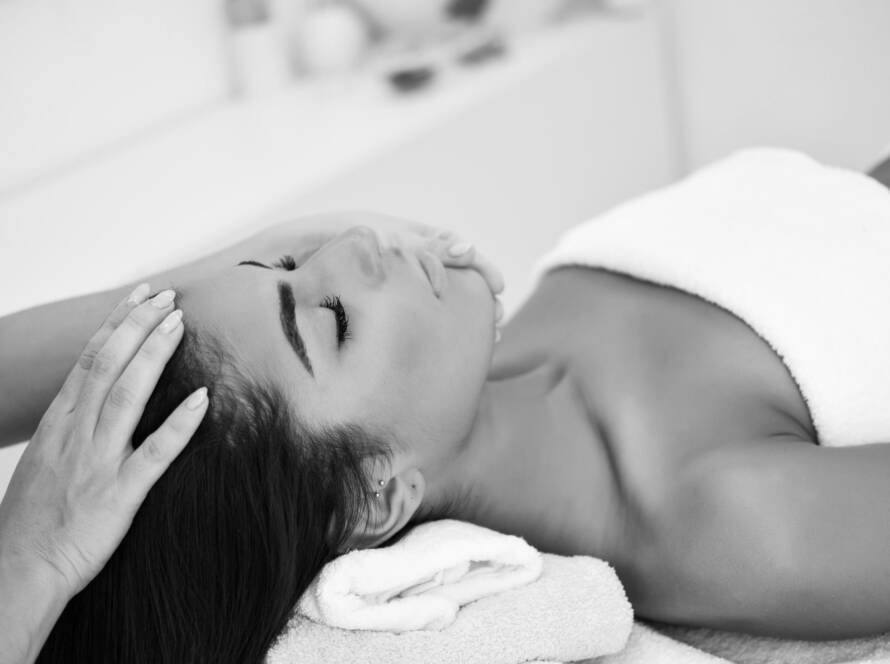 Black and white image of a woman on her back, looking very relaxed while the massage therapist has one hand on the top of the clients head and one under her chin, during an Indian head massage.
